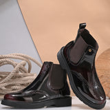 A glossy burgundy Chelsea boot with brogue detailing, elastic side panels, and a durable black sole, featuring a gold accent logo.