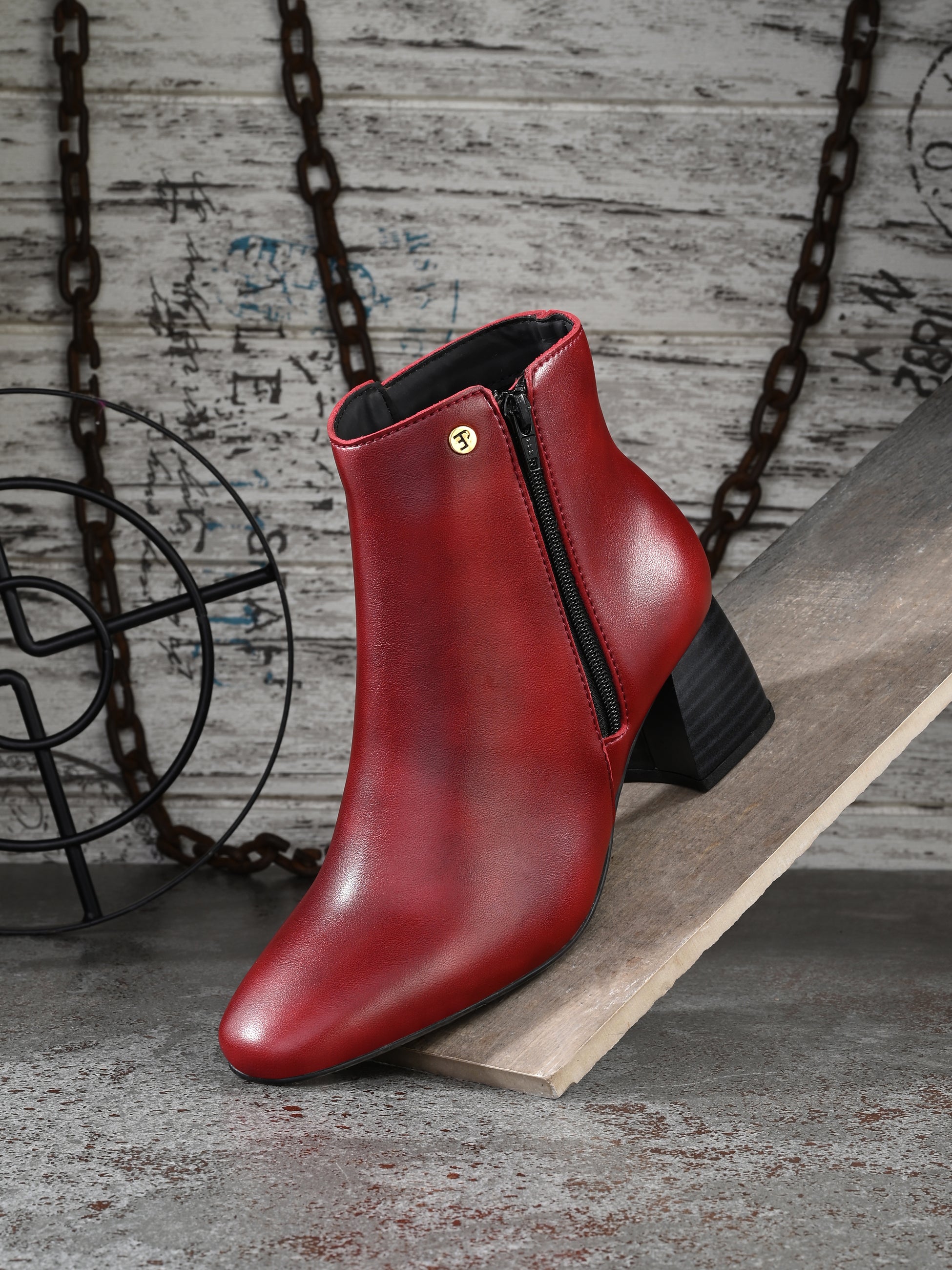 Suede ankle boot with pointed toe, chunky block heel, side zipper, and gold logo detail near the top.