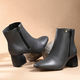 Suede ankle boot with pointed toe, chunky block heel, side zipper, and gold logo detail near the top.