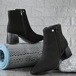 Suede ankle boot with pointed toe, chunky block heel, side zipper, and gold logo detail near the top.