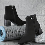 Suede ankle boot with pointed toe, chunky block heel, side zipper, and gold logo detail near the top.