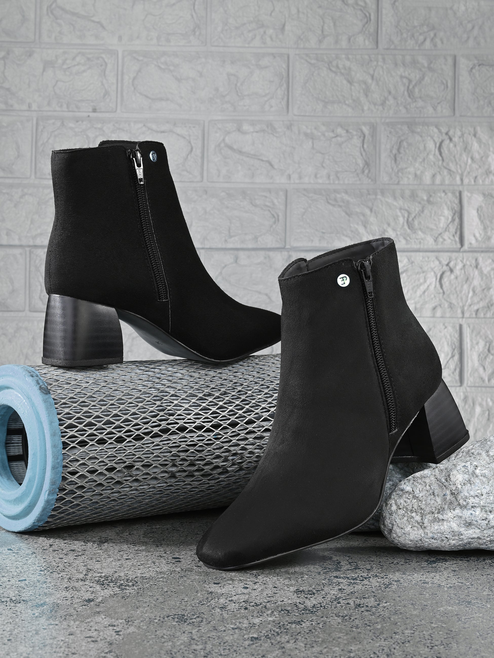 Suede ankle boot with pointed toe, chunky block heel, side zipper, and gold logo detail near the top.