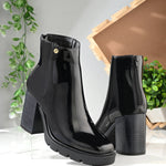 Glossy black patent leather zip-closure ankle boot with a chunky block heel, lug sole, and a gold logo detail near the collar.