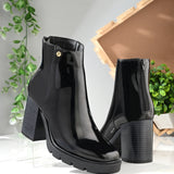 Glossy black patent leather zip-closure ankle boot with a chunky block heel, lug sole, and a gold logo detail near the collar.