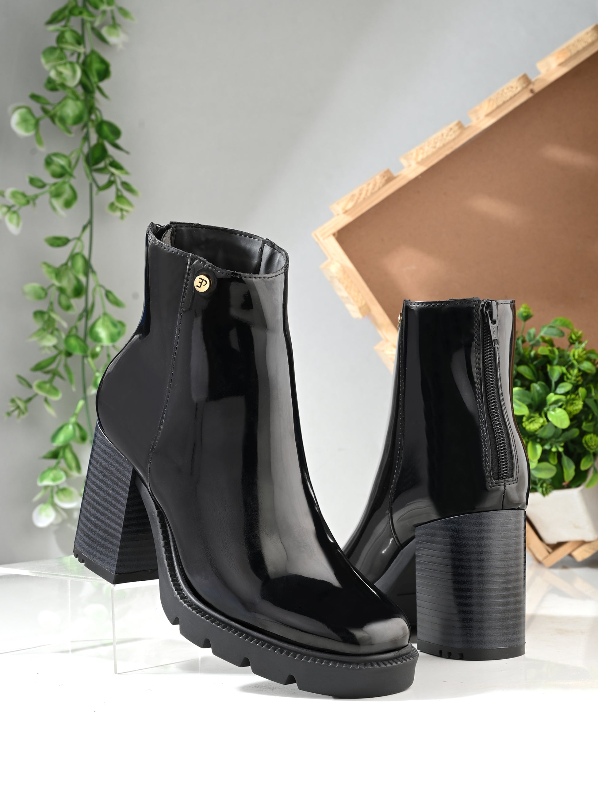 Glossy black patent leather zip-closure ankle boot with a chunky block heel, lug sole, and a gold logo detail near the collar.