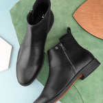 A sleek black leather Chelsea boot with a side zipper, pull-tab at the back, and a low block heel.