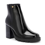 Glossy black patent leather ankle boot with a chunky block heel, lug sole, and a gold logo detail near the collar.
