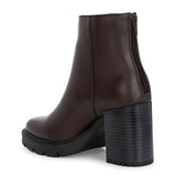 Glossy brown patent leather ankle boot with a chunky block heel, lug sole, and a gold logo detail near the collar.