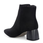 Suede ankle boot with pointed toe, chunky block heel, side zipper, and gold logo detail near the top.