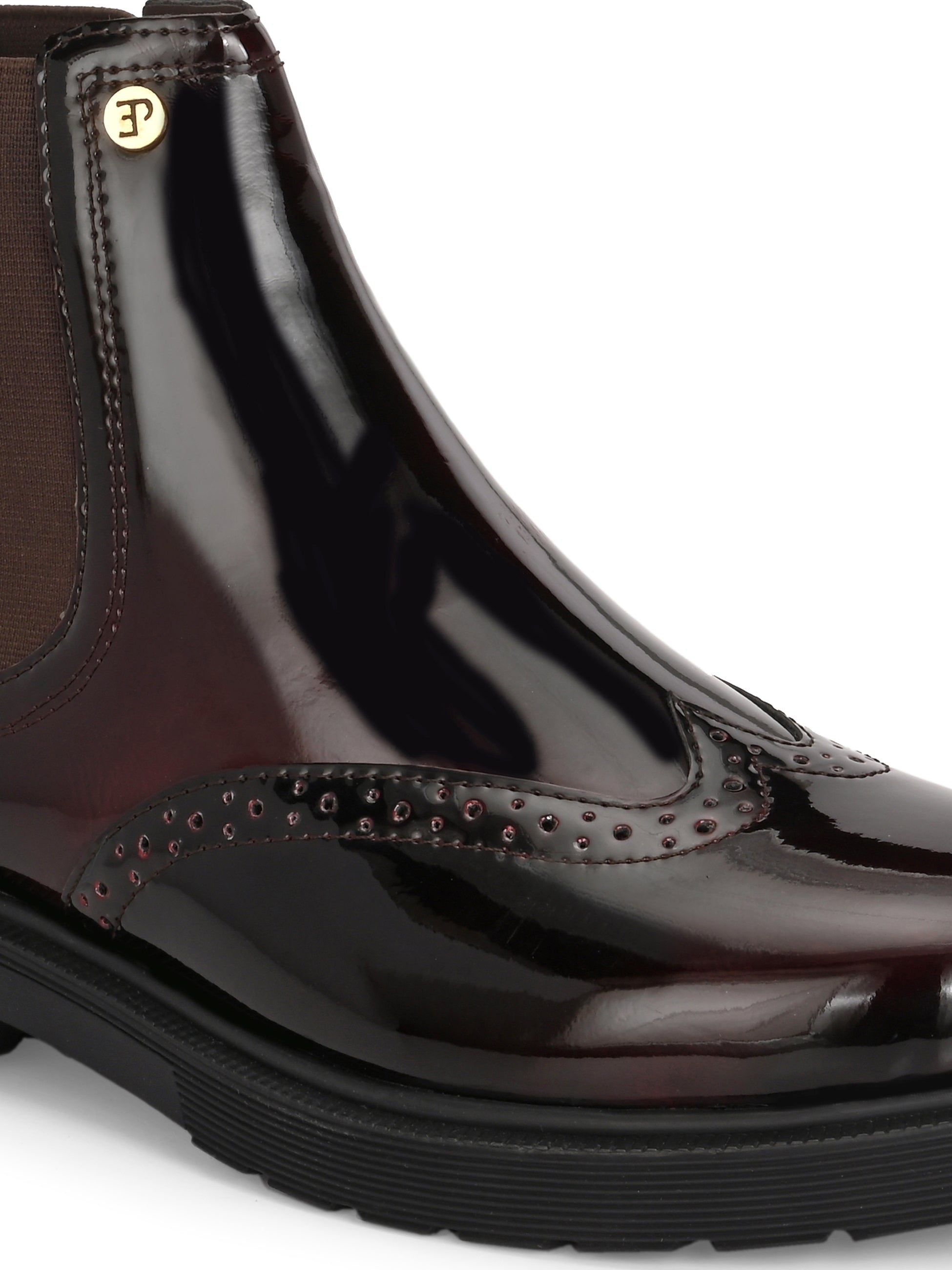 A glossy Wine Chelsea boot with brogue detailing, elastic side panels, and a durable black sole, featuring a gold accent logo.