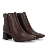 Suede ankle boot with pointed toe, chunky block heel, side zipper, and gold logo detail near the top.