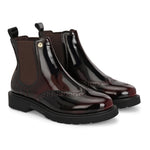 A glossy burgundy Chelsea boot with brogue detailing, elastic side panels, and a durable black sole, featuring a gold accent logo.