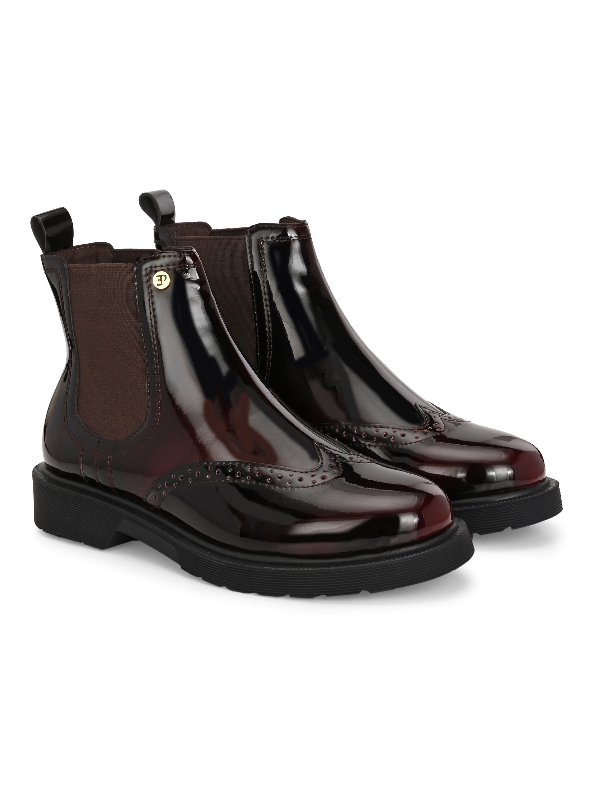 A glossy burgundy Chelsea boot with brogue detailing, elastic side panels, and a durable black sole, featuring a gold accent logo.