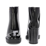 Glossy black patent leather ankle boot with a chunky block heel, lug sole, and a gold logo detail near the collar.