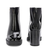 Glossy black patent leather ankle boot with a chunky block heel, lug sole, and a gold logo detail near the collar.