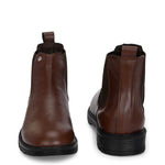 Brown Chelsea boots with elastic side panels, a pull-tab at the heel, rounded toe, and a small metallic brand logo near the ankle.
