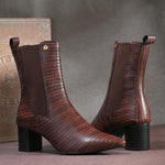 A sleek Tan crocodile-textured ankle boot with a pointed toe and mid-block heel, featuring an elastic side panel and a gold accent logo.