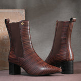 A sleek Tan crocodile-textured ankle boot with a pointed toe and mid-block heel, featuring an elastic side panel and a gold accent logo.