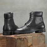 Men's black high-top lace-up boots with textured leather, padded collar, metal eyelets, and a rugged sole.