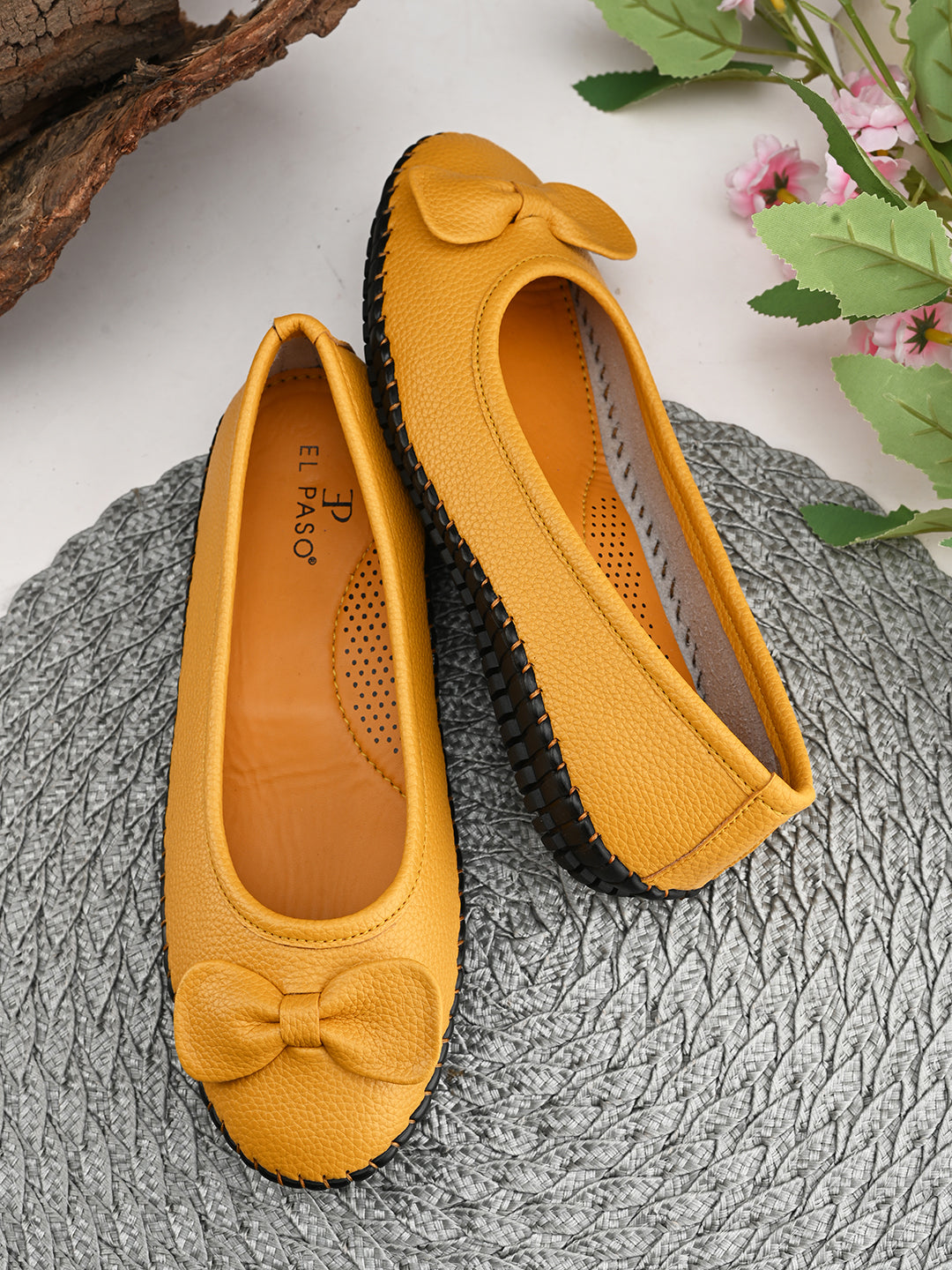 Mustard yellow leather Women Ballerina Flats with a decorative bow, black textured sole, and visible stitching for a casual, stylish look.