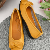 Mustard yellow leather Women Ballerina Flats with a decorative bow, black textured sole, and visible stitching for a casual, stylish look.