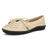 A beige women's flat with a perforated woven upper, round toe, metallic-tipped bow, and flexible black rubber outsole for comfort and casual wear.